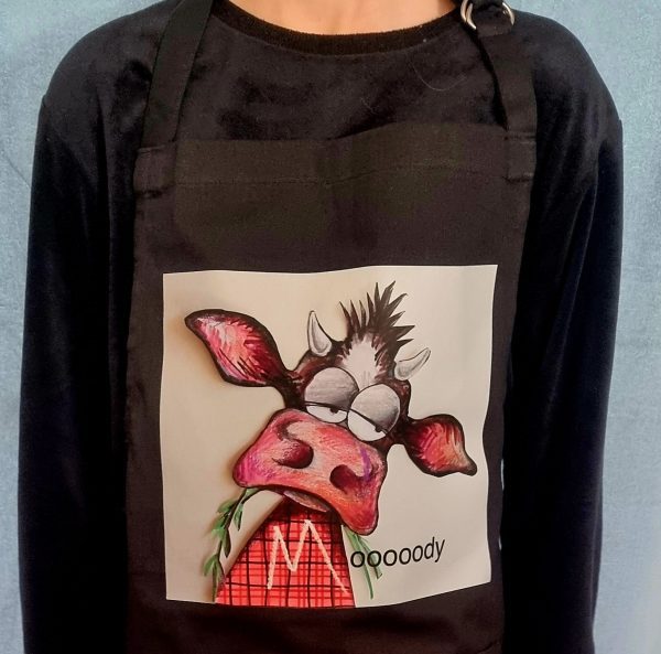 Black apron featuring a grumpy Highland cow cartoon in tartan with the word “Mooooody”
