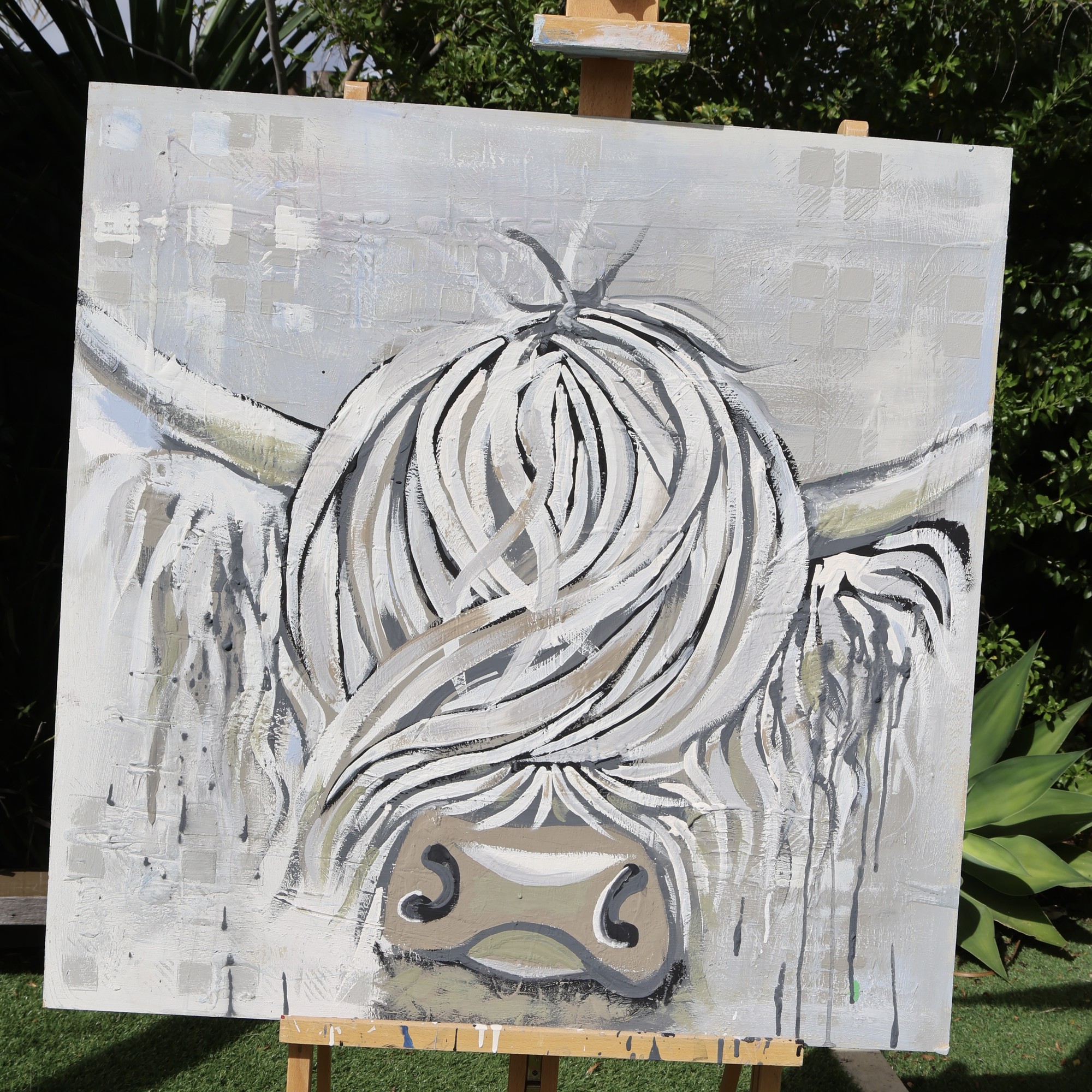 Iona, an original square Highland cow painting by Tartan Paint, unframed on a painting easel in the garden