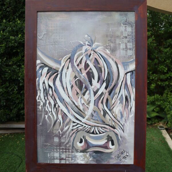 Isla, an original Highland cow painting in white, dusky pink, slate blue and mauve by Caroline Speirs, in a dark red timber frame on an easel in her Perth garden