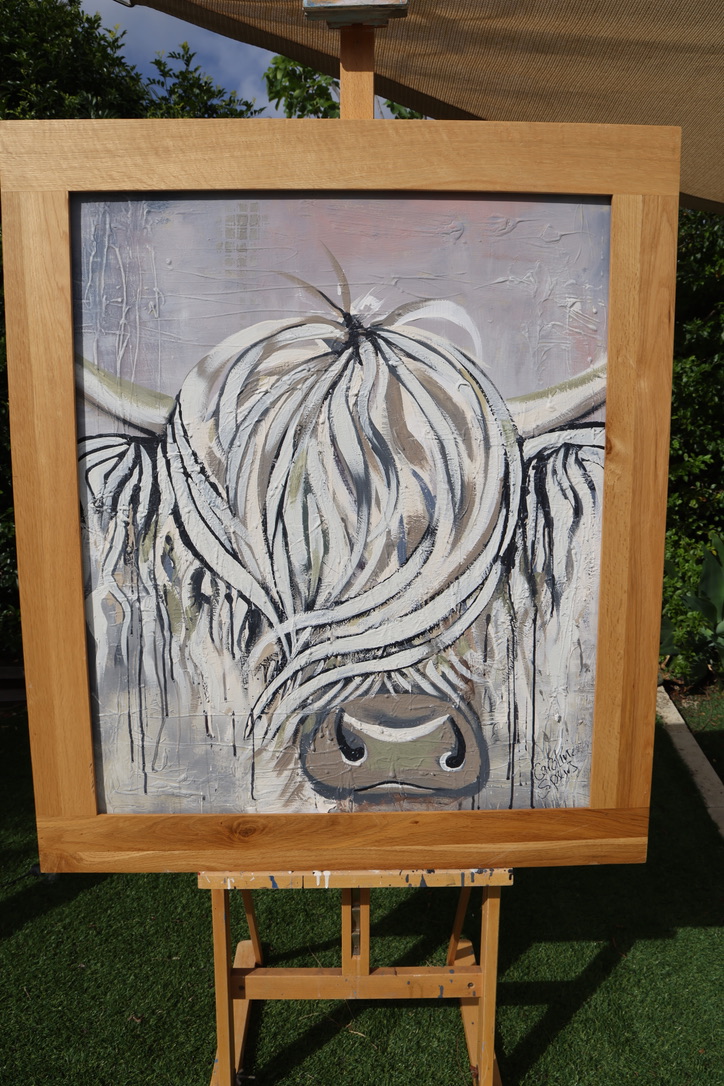 Moira, an original white and stone Highland cow painting with a blush pink sky and black drips, signed Caroline Speirs, framed in light oak