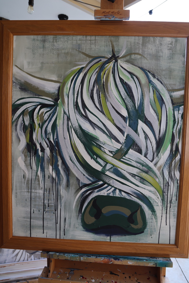 Paddy, an original Highland cow painting in white, forest green and lime with a deep green nose, framed in oak on a studio easel