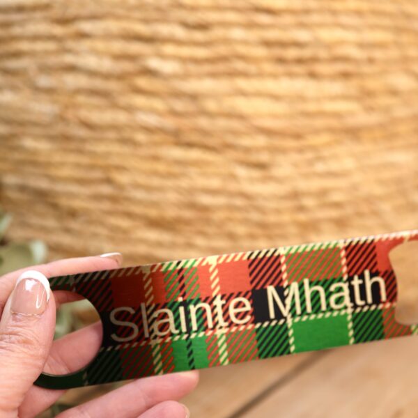 Slainte Mhath bar blade bottle opener on red and green tartan held in a hand